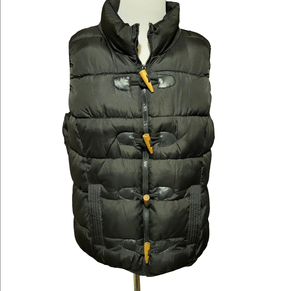 Large black puffer vest featuring a high collar,zipper,wooden toggle closure.